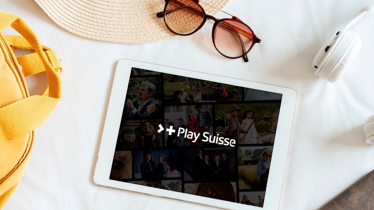 Tablet mit Playsuisse-Logo, Sonnenbrille, Kopfhörer, Sonnenhut und gelber Strandtasche